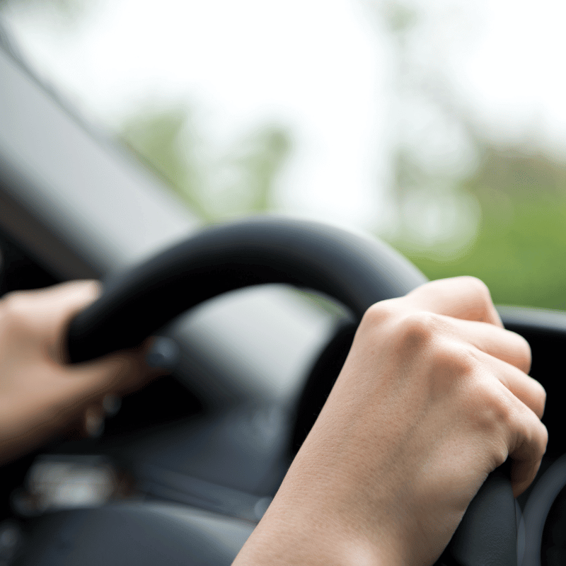 Women's hands on the steering wheel of a car.