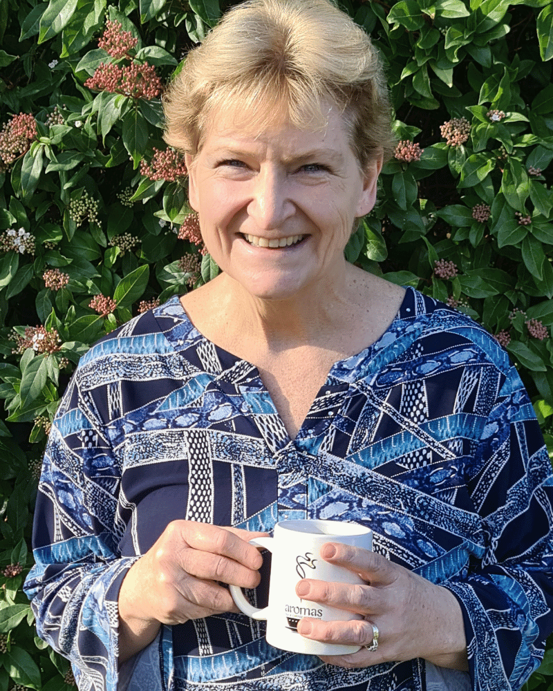 Sue standing outside holding a cup of coffee.